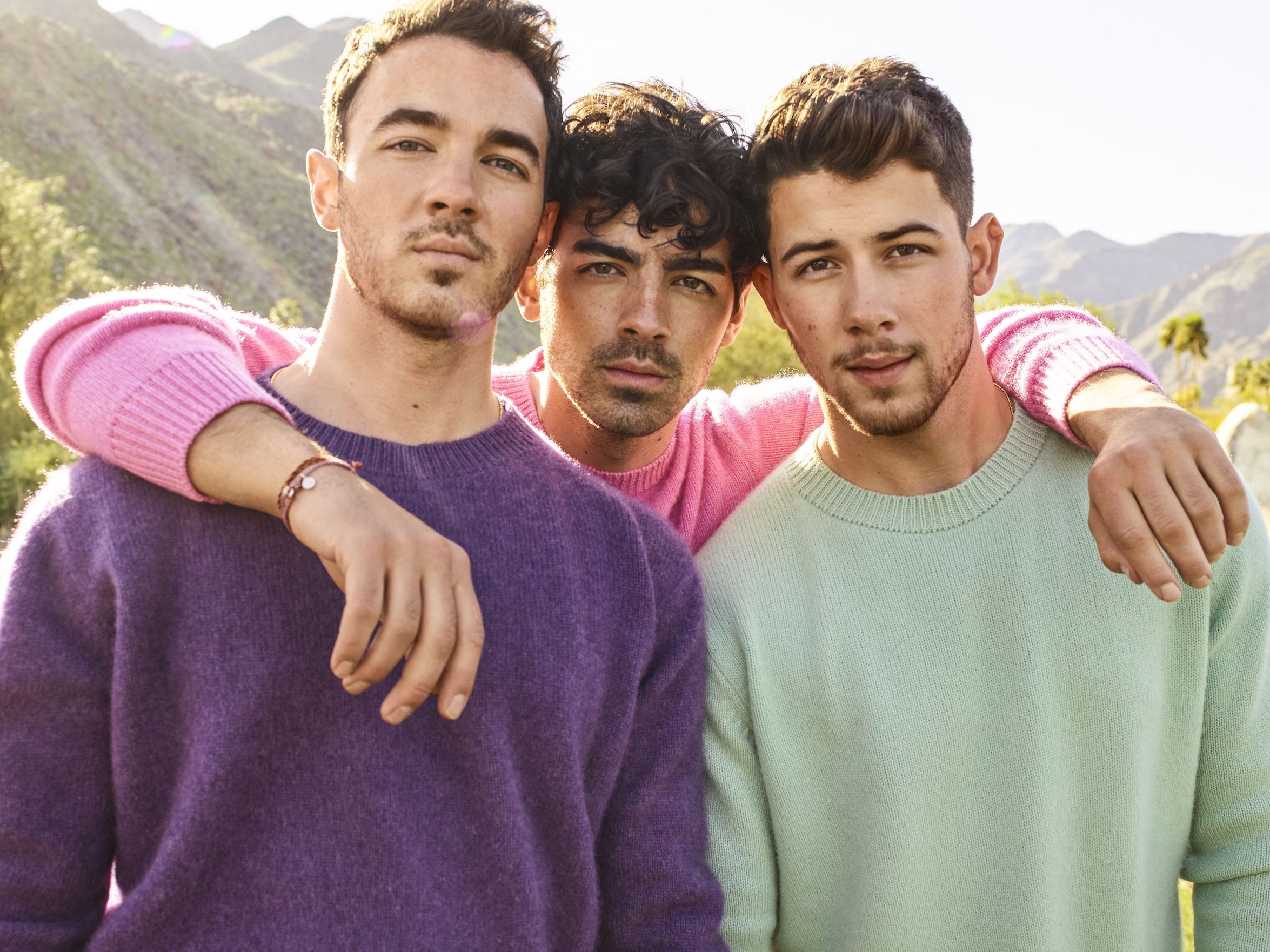Os irmãos Kevin, Joe e Nick Jonas posam para foto, olhando diretamente para a lente, com montanhas naturais ao fundo