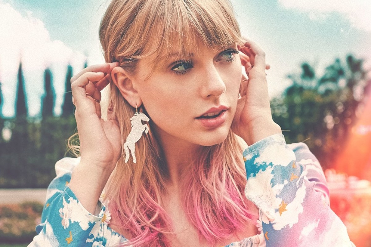 Com mechas rosas no cabelo e um brinco de unicórnio, Taylor Swift posa, olhando pro lado